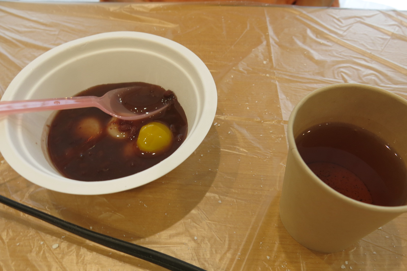 左側に白い器の中に白玉の入ったおしるこ、右側には紙コップにほうじ茶、の写真