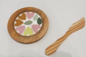 左に丸いコースター。中央にピンクやオレンジなどのハート形で葉っぱを囲むようにタイルが並べられています。右にバターナイフがあります。