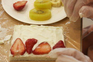 生クリームを塗った食パンに果物を並べている写真。パンの左端にイチゴが4枚並べられている。